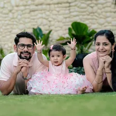 So much joy in one picture! A happy baby girl raises her hands while lying on the grass with her loving parents for a beautiful family portrait.
