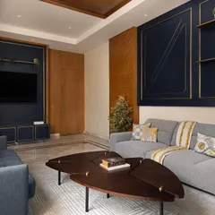 In the Prata House, modern luxury is achieved through bold color choices and clean lines. The living room features a deep blue wall with geometric brass inlays, creating a sophisticated backdrop for the comfortable, modern sectional sofa.