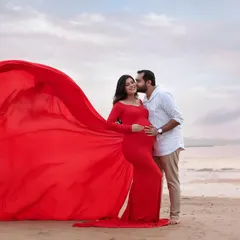 A portrait of love and joy by the ocean. His sweet kiss and the dramatic sweep of her red gown make this a truly cinematic and romantic maternity photo.