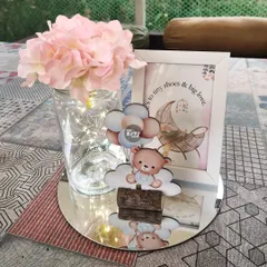 This sweet centerpiece captures the essence of a teddy bear theme. It features a cute bear and balloon cutout, a framed print with a heartfelt quote, and a baby shoe holding delicate flowers, all arranged on a mirrored tray.