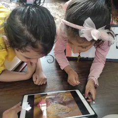 Learning starts with observation. Here, two curious students study a butterfly on a tablet before starting their own drawings, connecting art with the natural world.
