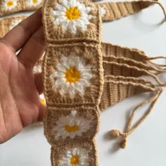 A close up of the crochet headband, showing the detail of the daisy squares and the tapered ends with ties for an adjustable fit.