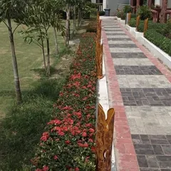 This project shows a pathway in a commercial or public area lined with a dense hedge of red Ixora flowers. The design adds a vibrant splash of color and is bordered by decorative wooden posts.
