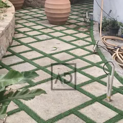 Here you can see how the artificial grass grid pattern follows the curve of the garden path, creating a visually interesting and low-maintenance surface that combines hardscape with greenery.