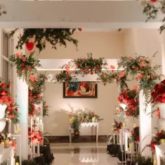An elegant floral archway welcomes guests to the wedding. The beautiful arrangement of red and green florals against a white structure creates a stunning entrance and a perfect photo opportunity.