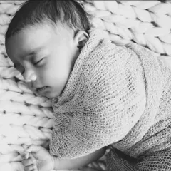 A peaceful newborn sleeps soundly, swaddled in a soft, chunky knit blanket. This black and white photo emphasizes the serene and delicate nature of your baby's first days.