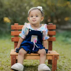 A cute portrait of a little girl sitting on a bench in the park, with a sweet, curious expression.