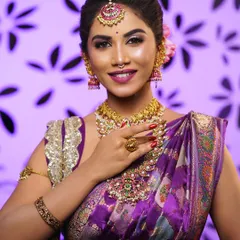 A close-up of a flawless HD bridal makeup look. Notice the smooth skin finish, the perfectly blended cut-crease eyeshadow, and how the makeup harmonizes with the bride's purple silk saree and temple jewellery.