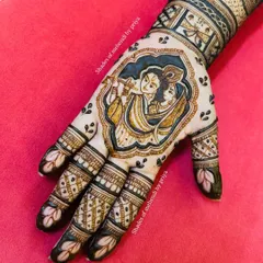 A stunning Radha Krishna portrait nestled in the palm of a bridal mehendi. The use of dark, bold lines makes the divine couple the centerpiece of the design.