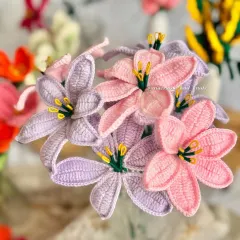 A close-up of the lavender and baby pink crochet lilies. The soft colors and detailed stitching on the petals and stamens make them look so delicate and real.