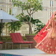 A stunning bridal portrait by the pool. The bride's magnificent red lehenga and the graceful movement of her veil create a dramatic and beautiful image.