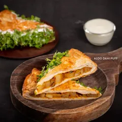 Meet the legend: our Aloo Dahi Puff. It's a unique creation with a flaky, golden crust filled with a tangy potato and yogurt mix, then topped with fresh coriander. It’s the perfect savory snack.