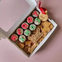 The 'Merry X-mas' mini cupcakes box. It includes cupcakes spelling out the festive message, assorted Christmas-themed cookies, and a personalised name tag ornament.