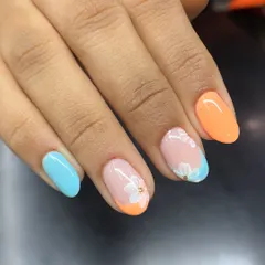 A relaxing holiday vibe on your nails. This design combines a classic French with a twist, using pastel orange and blue tips and a delicate white flower accent.