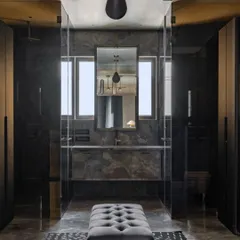 The master bathroom at Aikaa, featuring dark marble and dramatic lighting. The central ottoman adds a touch of softness and provides a place to sit, enhancing the room's spa-like feel.