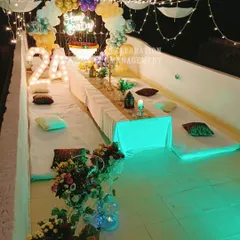 A vibrant terrace party setup for a 24th birthday. This features low seating, marquee numbers, a neon sign, and even umbrellas integrated into the fairy light ceiling for a unique touch.