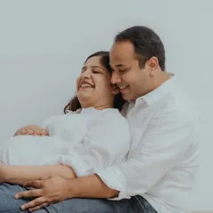 Pure, unscripted happiness. This candid photo captures the couple sharing a laugh, highlighting the easygoing and comfortable atmosphere of a lifestyle maternity session at home.