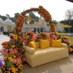 A vibrant Haldi seating area bursting with colorful flowers. The mix of orange, yellow, and pink creates a joyful and energetic atmosphere.