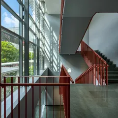A staircase with bright red railings set against a large glass wall, allowing natural light to flood the space. This design shows how transitional elements can engage with light and materiality to define a building's character.