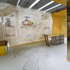 The reception area at the AMG office features an architectural plan imprinted on the floor, creating a visual dialogue with the conceptual drawings on the wall. This approach celebrates the design process, turning the entrance into a narrative space.