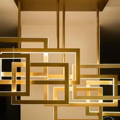 This modern architectural chandelier features an array of interlocking geometric squares with a brushed gold finish. The integrated LED lighting provides a warm, ambient glow, making it a sophisticated centerpiece for contemporary dining rooms and living spaces.