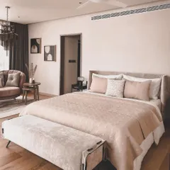 A spacious and luxurious master bedroom featuring a soft, muted color palette, a comfortable seating nook, and elegant furnishings for a hotel-like feel.