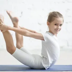 A young student holds the bow pose, or Dhanurasana, an essential exercise for developing back flexibility and opening the chest. This foundational yoga-based stretch is a key part of our warm-up and conditioning for young gymnasts.