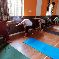 Participants perform a deep side-body stretch while seated on chairs. This pose is excellent for releasing tension in the shoulders and back, common issues for office workers.