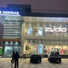 The finished "The Sidewalk" building at dusk, with the Zudio showroom brightly lit. The modern facade I designed gives it a strong commercial presence.