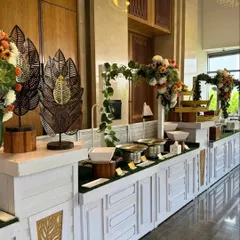 A clean, contemporary buffet design featuring white panelled counters, lush greenery, and artistic metal leaf sculptures. This setup is ideal for modern corporate events that require a touch of understated elegance.