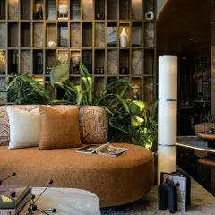 Detail of the lounge seating, highlighting the custom-patterned upholstery and the sculptural floor lamp. The backlit grid wall serves as both a bookshelf and a mood board, adding layers of texture and personality.