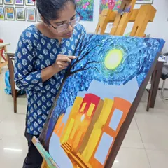 A student applies textured layers to her night scene painting. This image shows the hands-on process of building up a composition with a palette knife for a rich, tactile effect.
