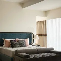This guest bedroom features a bold blue headboard and a tufted dark grey ottoman. The design is clean and modern, with a focus on comfort and a serene color palette.