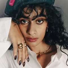 This close-up shot highlights multiple accessories at once: the rings, necklace, and nail polish. The model's hand is posed elegantly to display the jewelry naturally. The lighting is soft yet directional, bringing out the shine of the gold and the deep color of the nails.
