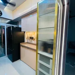 A tall pantry or crockery unit with a fluted glass door and a striking gold-finished frame. The unit is lit from within, turning everyday storage into a beautiful display feature in the kitchen.