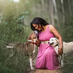 A duplicate of image 65, this image perfectly captures the affectionate bond between a pet parent and her rescue dogs. The natural, green environment and soft lighting create a peaceful atmosphere for this beautiful interaction.