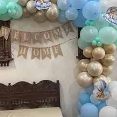 A lovely "Welcome Home" setup for a baby boy. This decor features a rustic burlap banner and a beautiful organic balloon arch in shades of baby blue, mint green, and gold, creating a warm and inviting atmosphere.