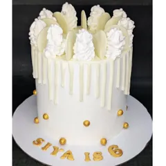 A tall, all-white cake for a white-themed birthday party. This choco-chip cake features a white chocolate drip and is accented with gold spheres for a touch of elegance.