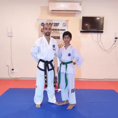 A student stands proudly with his coach after successfully passing his belt grading exam and earning his new green belt.