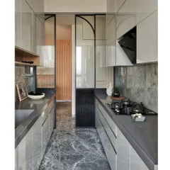 This sleek, modern galley kitchen features high-gloss grey cabinets and a dramatic marble floor. The design uses reflective surfaces to make the narrow space feel larger, while the glass partition maintains a connection to the rest of the home.