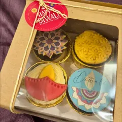 A box of four intricately designed Diwali-themed cupcakes. Each one features a unique edible topper, from a diya to a rangoli pattern, making it a beautiful and delicious gift.