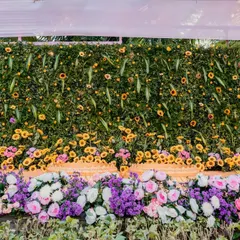 A stunning floral wall created for a Haldi ceremony. The dense arrangement of greenery, sunflowers, and other colorful blooms serves as a vibrant and fresh backdrop for photos.