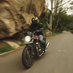 A rider on a Royal Enfield motorcycle navigates a winding road, with the motion blur giving a great sense of speed. This panning shot captures the thrill of riding through a scenic route.