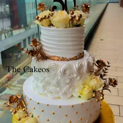 A grand three-tier cake designed for a 50th anniversary, combining different buttercream textures. The cake features a quilted bottom tier, a rosette middle tier, and a smooth top tier, all adorned with beautiful yellow and golden roses.