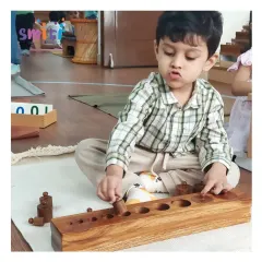 A child shows deep concentration while working with the Montessori knobbed cylinder block. This sensorial activity helps refine his visual discrimination of size and prepares him for writing by strengthening his pincer grip.