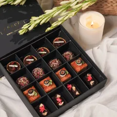 Our Rakhi Re-Imagined Box features sixteen handcrafted modern Indian sweet bites. This elegant gift box includes a delightful assortment of White Chocolate & Almond Cake, Cherry & Milk Chocolate Tarts, and our wholesome Roasted Almond & Whole Wheat Ladoos, perfect for sharing sweet moments.