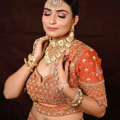 A moment of serenity. With her eyes closed, you can fully appreciate the beautiful blend of pink and rose gold eyeshadow, a perfect choice for a modern bride wearing a vibrant orange lehenga.