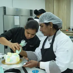 Here, I'm providing one-on-one guidance to a student, helping her perfect the angle and pressure for piping beautiful buttercream roses. This personalized attention is a core part of our teaching philosophy.