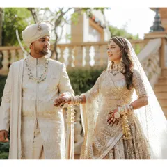 A classic couple portrait showcasing their stunning wedding day ensembles. The groom's layered pearl and emerald necklace perfectly complements the bride's choker, demonstrating a thoughtful approach to coordinated accessorizing.