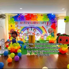A bright and colorful Cocomelon theme, perfect for a first birthday party. This setup includes a rainbow balloon arch, a full cast of character cutouts, and a large marquee number '1' for the perfect photo opportunity.
